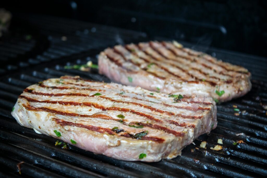 Close-up of succulent pork steaks sizzling on a barbecue grill. Perfect for culinary and barbecue themes.