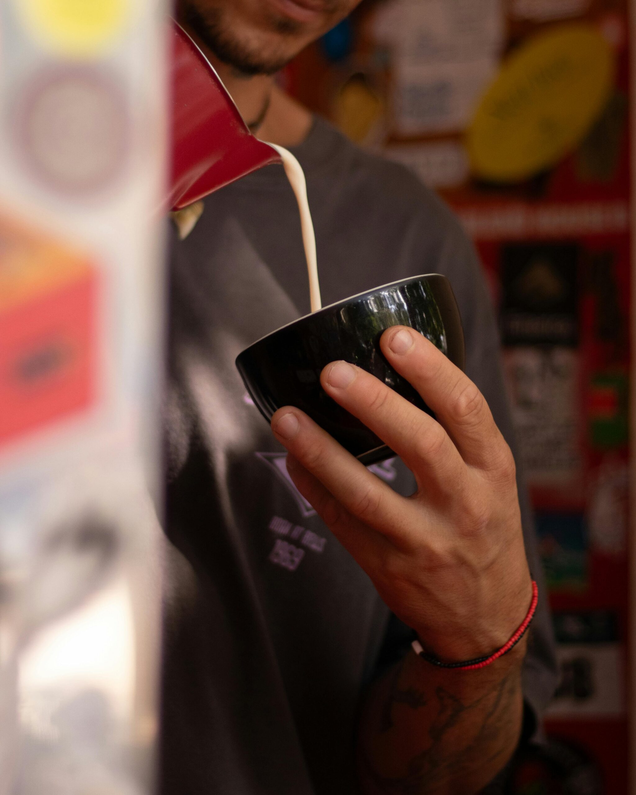 Close-up of person pouring iced coffee into a black ceramic cup. Vibrant background.